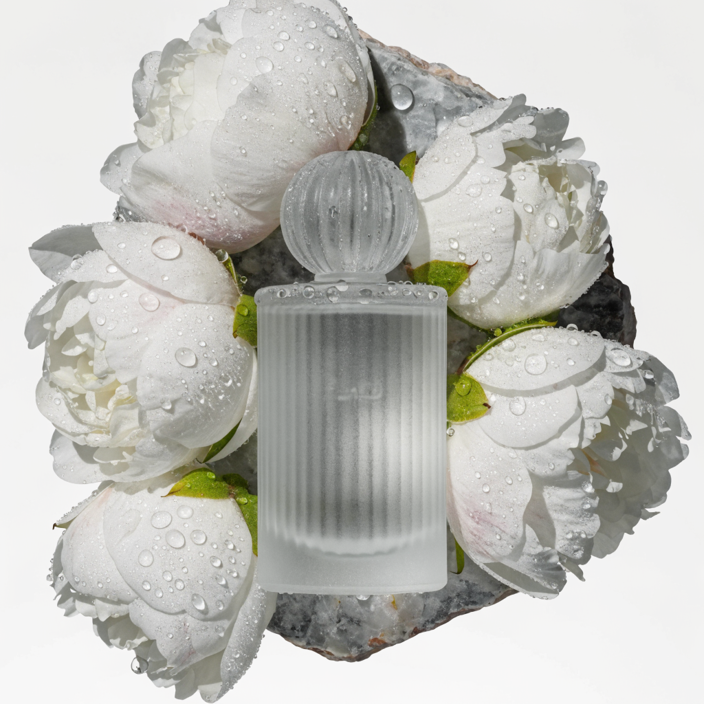 A frosted glass perfume bottle on a slab of raw marble, surrounded by scattered white