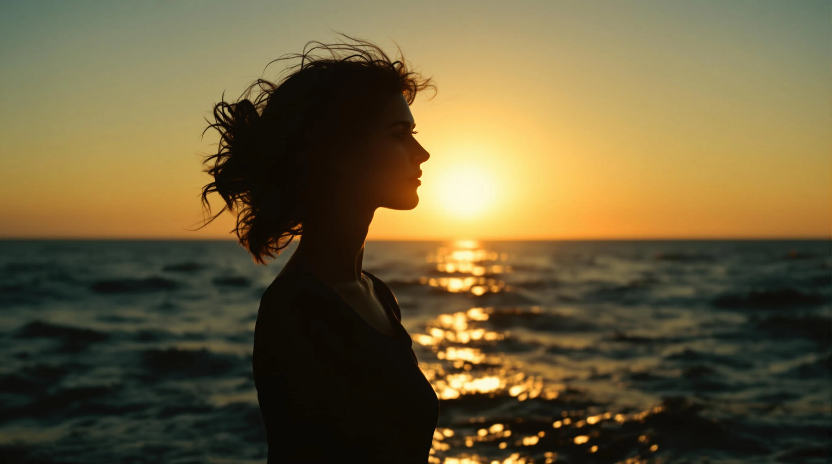 A cinematic silhouette of a woman standing still at the edge of the sea, framed by the golden-orange glow of a low-setting sun. Her hair is gently lifted by the breeze, and her figure is outlined crisply against the shimmering waves. The mood is reflective and timeless.