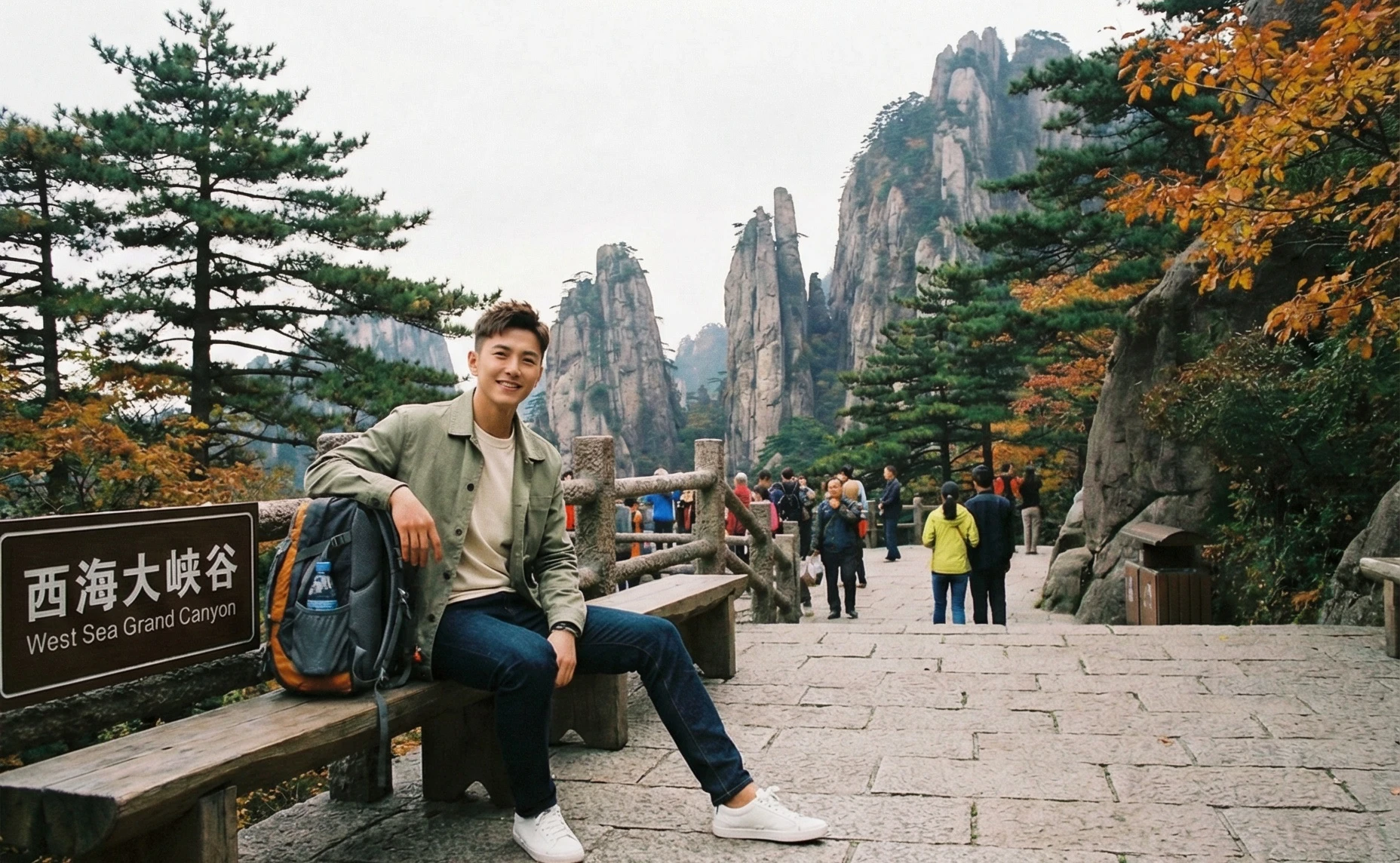 Photo-realistic edit of the reference photo. Keep the original West Sea Grand Canyon background, stone path, railings, autumn trees and tourists in the distance. Replace the elderly man on the bench with a handsome young male celebrity-looking man in his late 20s, stylish haircut, clear skin, natural smile, casual but fashionable outdoor outfit (light jacket, shirt, jeans, sneakers), holding a backpack beside him in a relaxed pose. Maintain the same camera angle and composition, soft daylight, realistic colors, high resolution travel photography style.